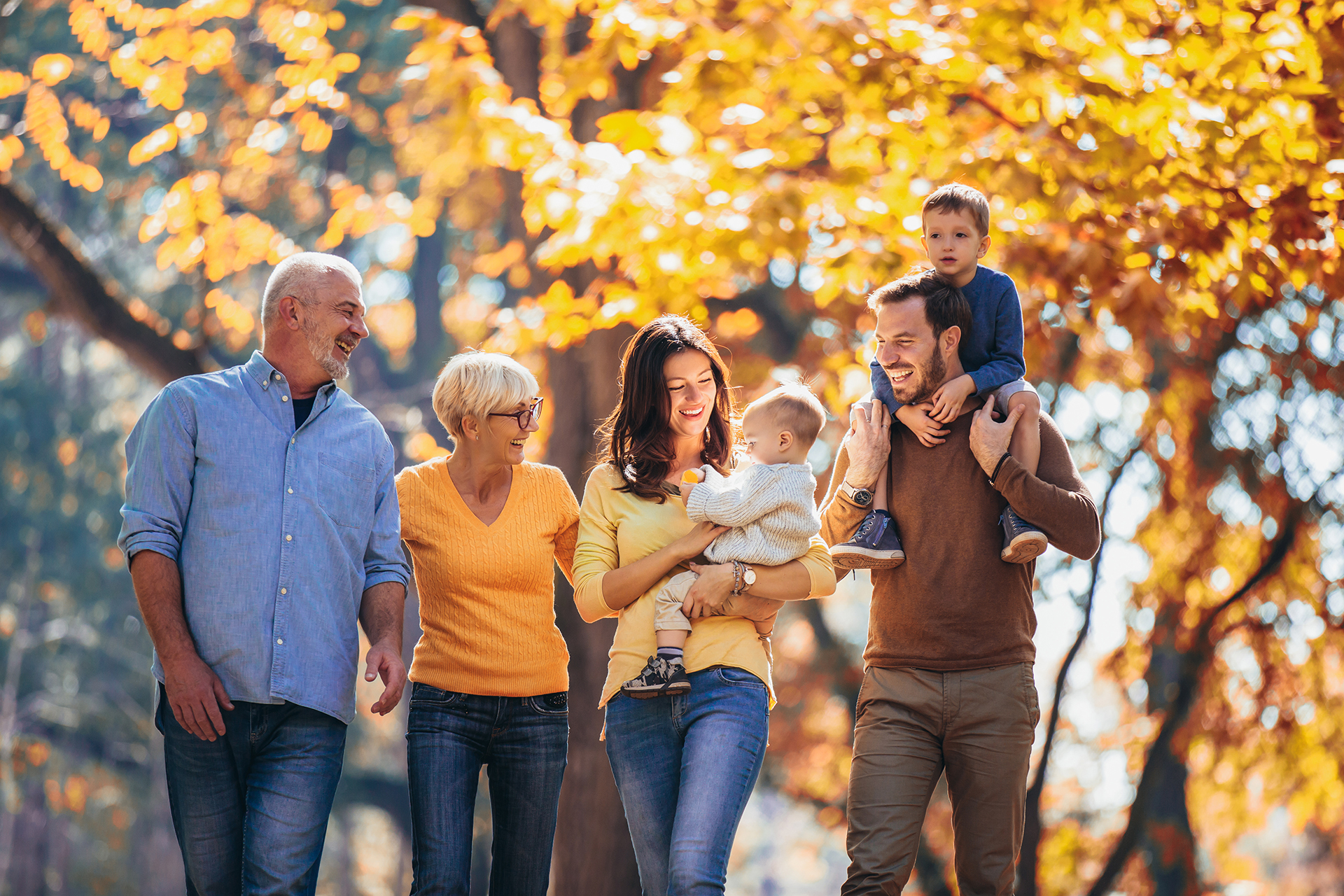 A multi-generational family takes a walk in a city park during the fall.